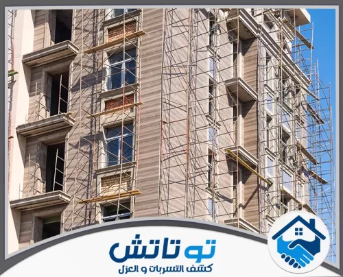 شركة تكسير وترميم مباني في عجمان 0565603382 شركة توتاتش واجهة بناية شاهقة تخضع للترميم والكساء، حيث تعانق السقالات جدرانها تحت ضوء الشمس